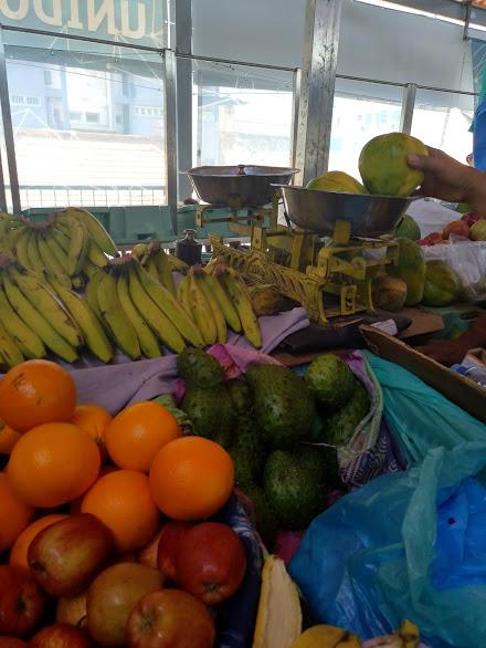 Banca com vários tipos de fruta: maçã, banana, laranja. No momento estão a ser pesadas papaias