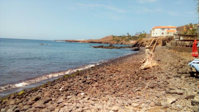 Praia de rochas com o mar e algumas casas.