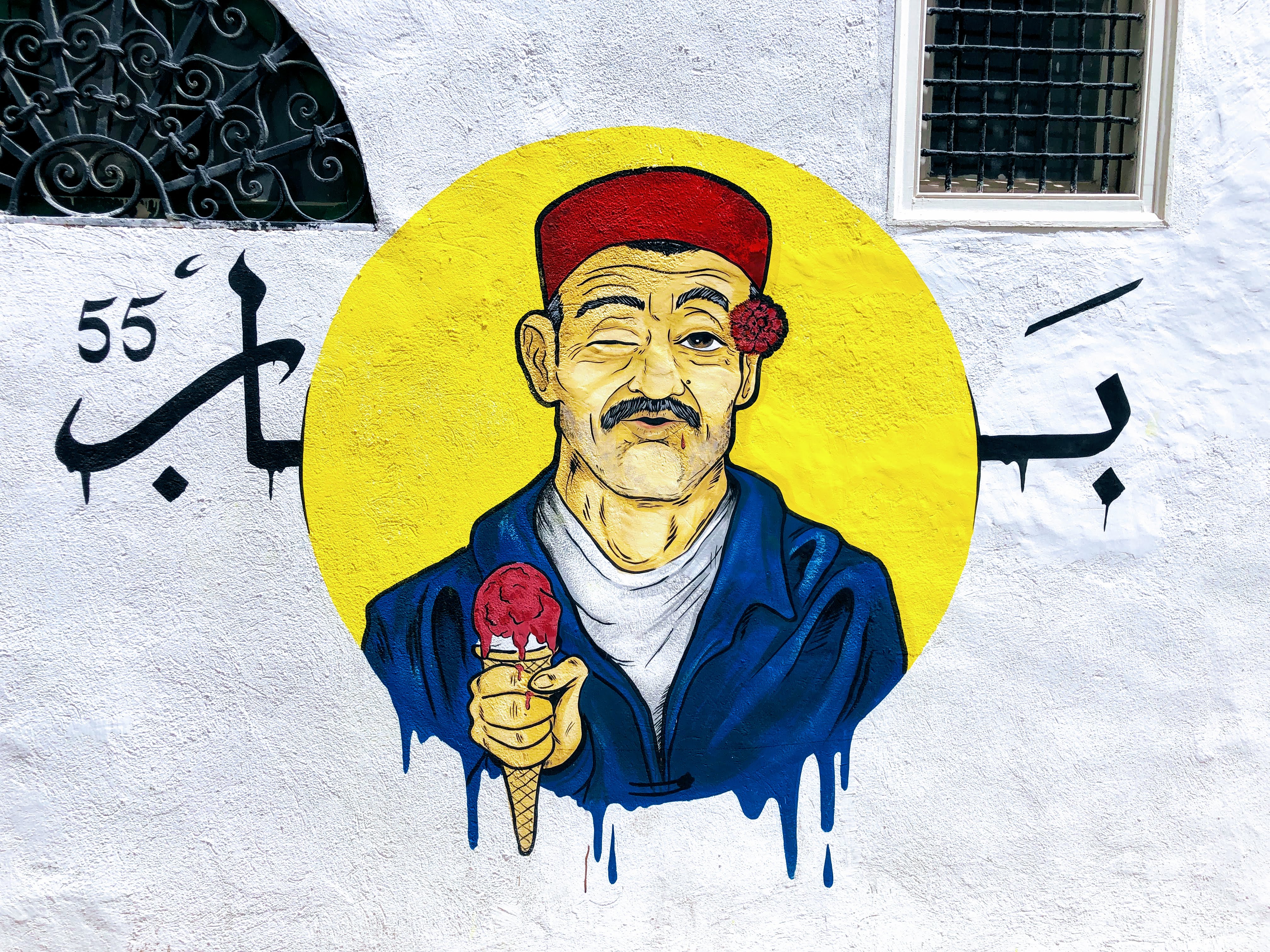 Street art: retrato de um tunisino tradicional, que usa uma chachia na sua cabeça, segura uma mechmoum na sua orelha e veste um dangri. Ao segurar um gelado, esta personagem representa a preservação da tradição pela comunidade jovem. 